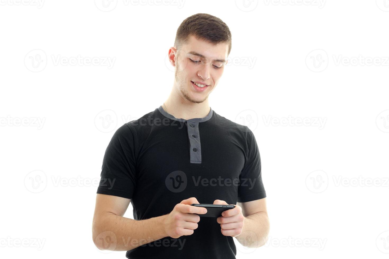 en leende ung man i en svart t-shirt är spelar på en mobil telefon foto