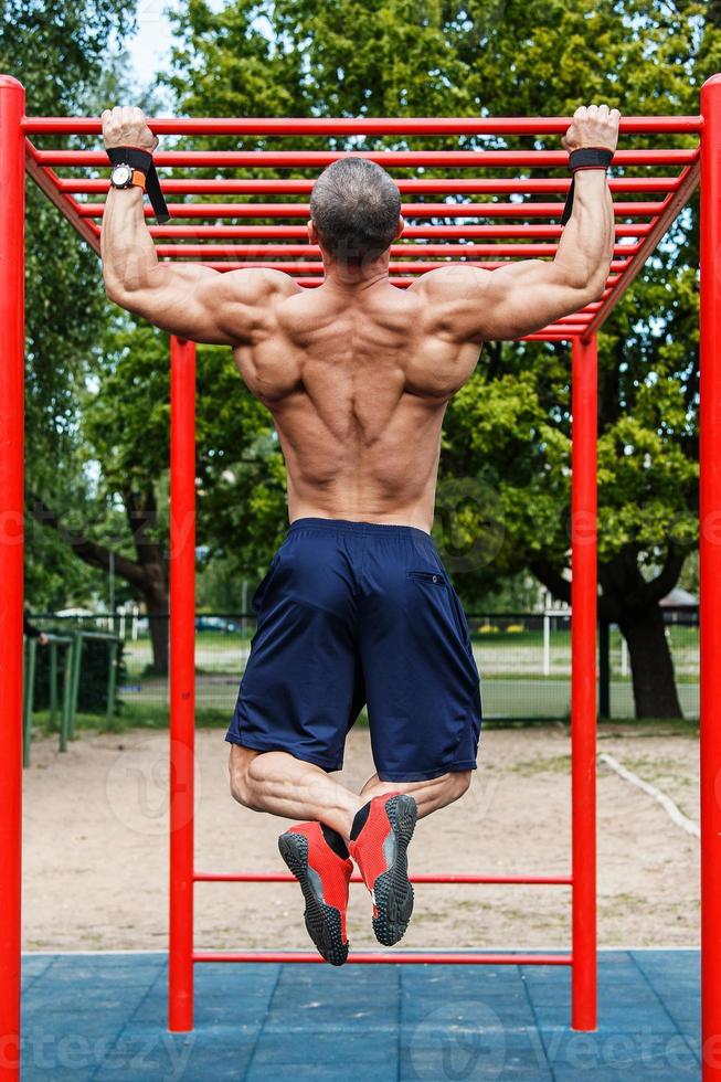 muskulös man håller på med pull-ups på horisontell bar foto