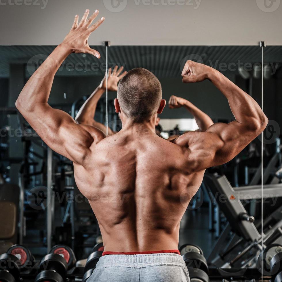 ung man som visar hans muskulös tillbaka i Gym foto