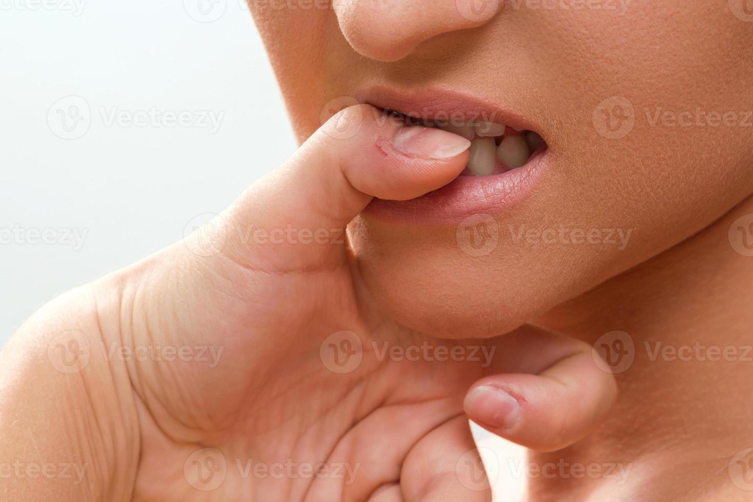 närbild av en kvinna mun bitande henne fingrar foto