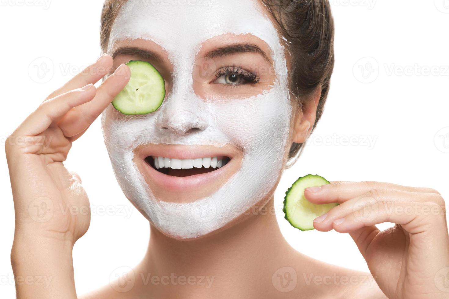 kvinna med ansiktsbehandling mask och gurka skivor i henne händer foto