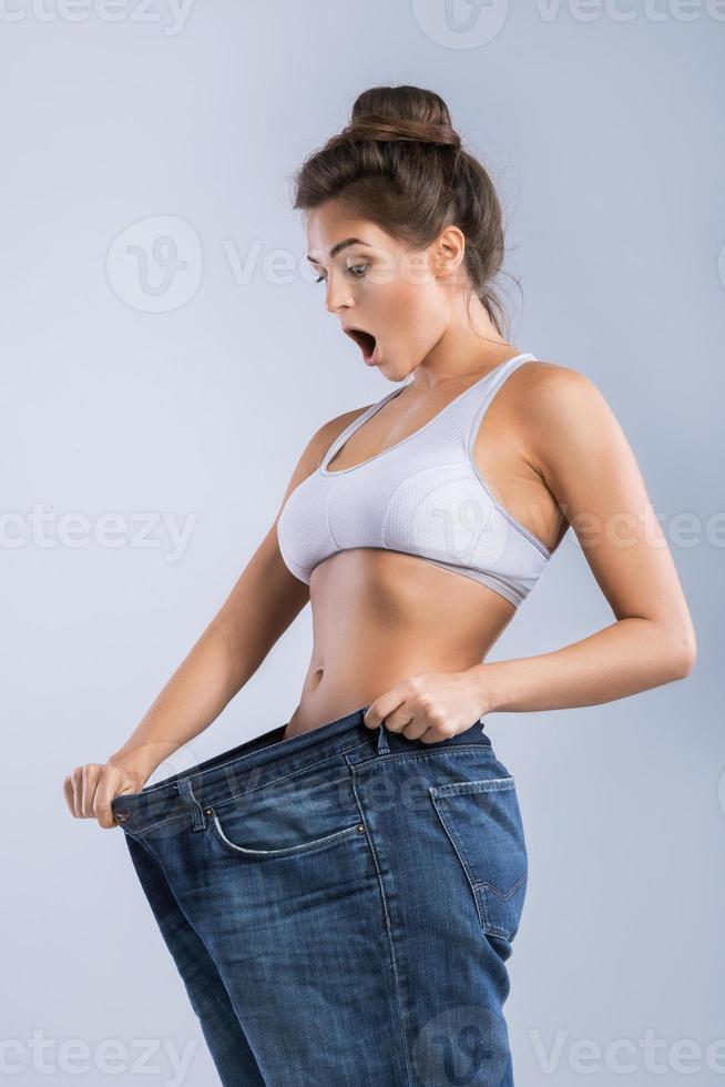 Lycklig kvinna bär jeans efter viktminskning på grå bakgrund foto
