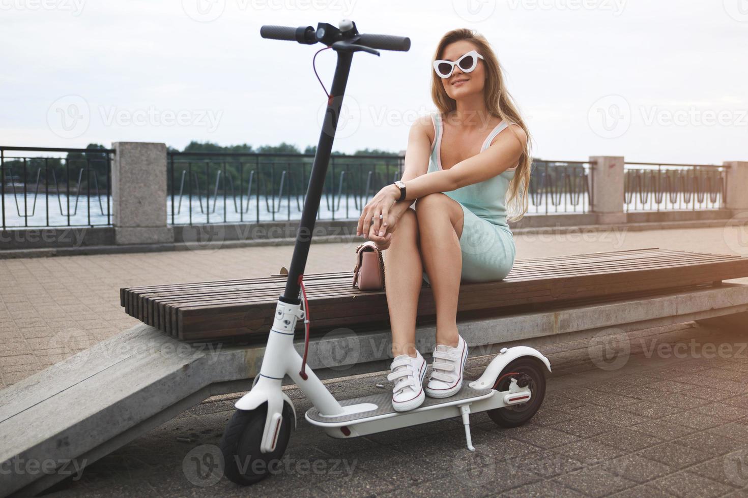 eleganta kvinna med elektrisk skoter på de flodstrand foto