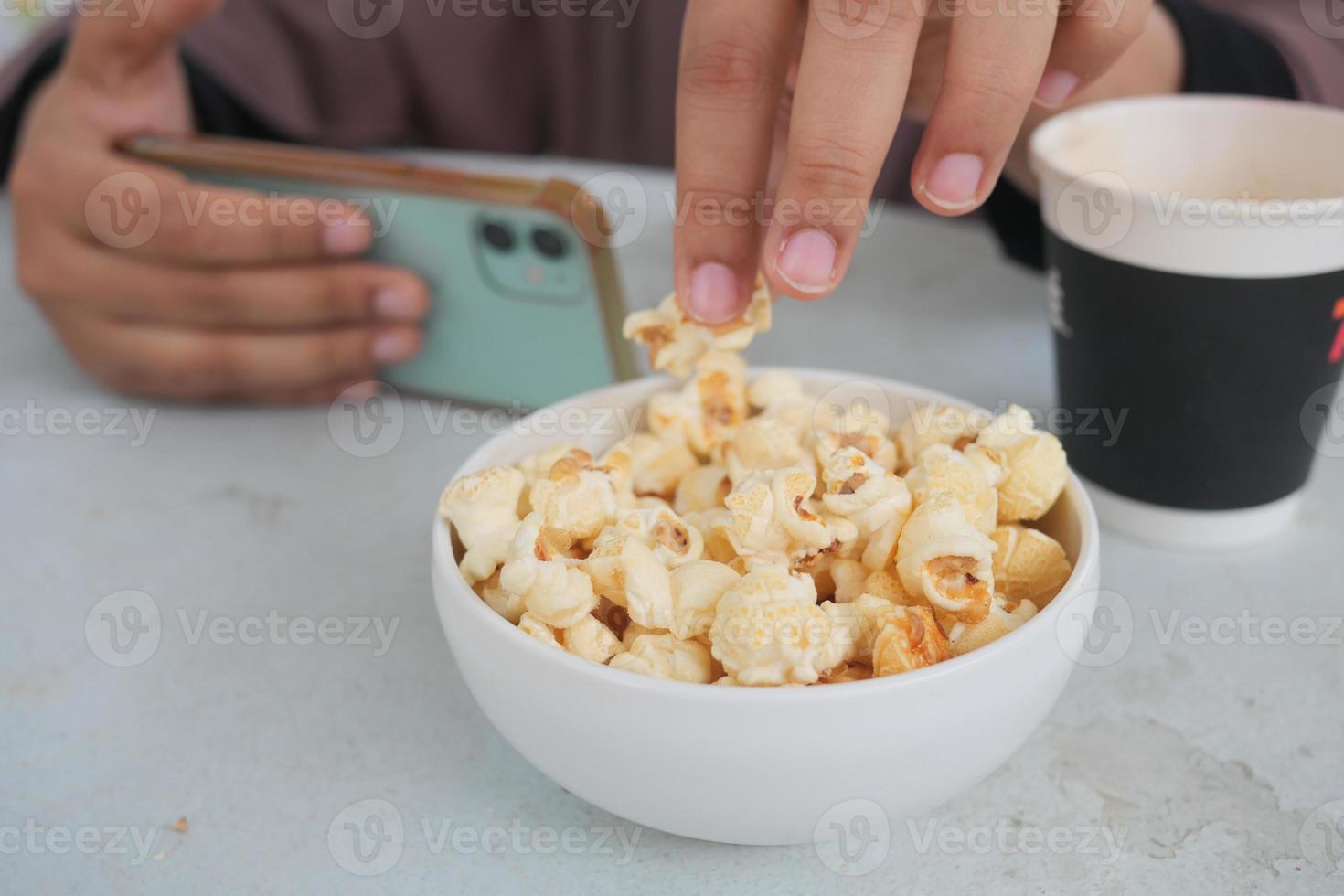 ung kvinnor äter popcorn och innehav en smart telefon foto