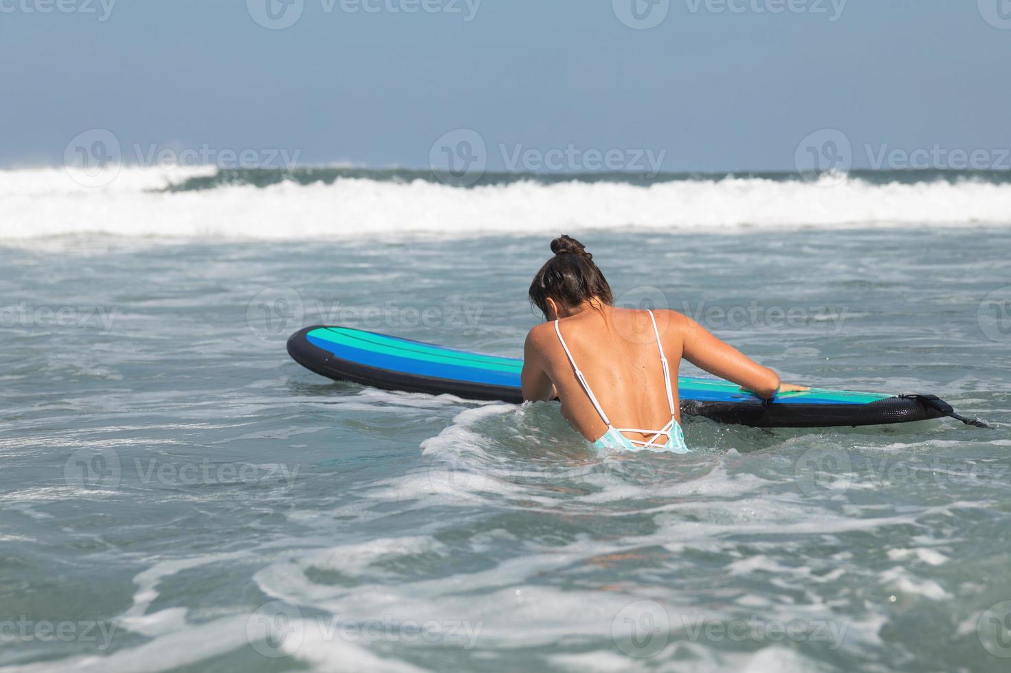 kvinna surfare är påfrestande till skaffa sig in i linje upp tråg vågor under henne surfing träna foto