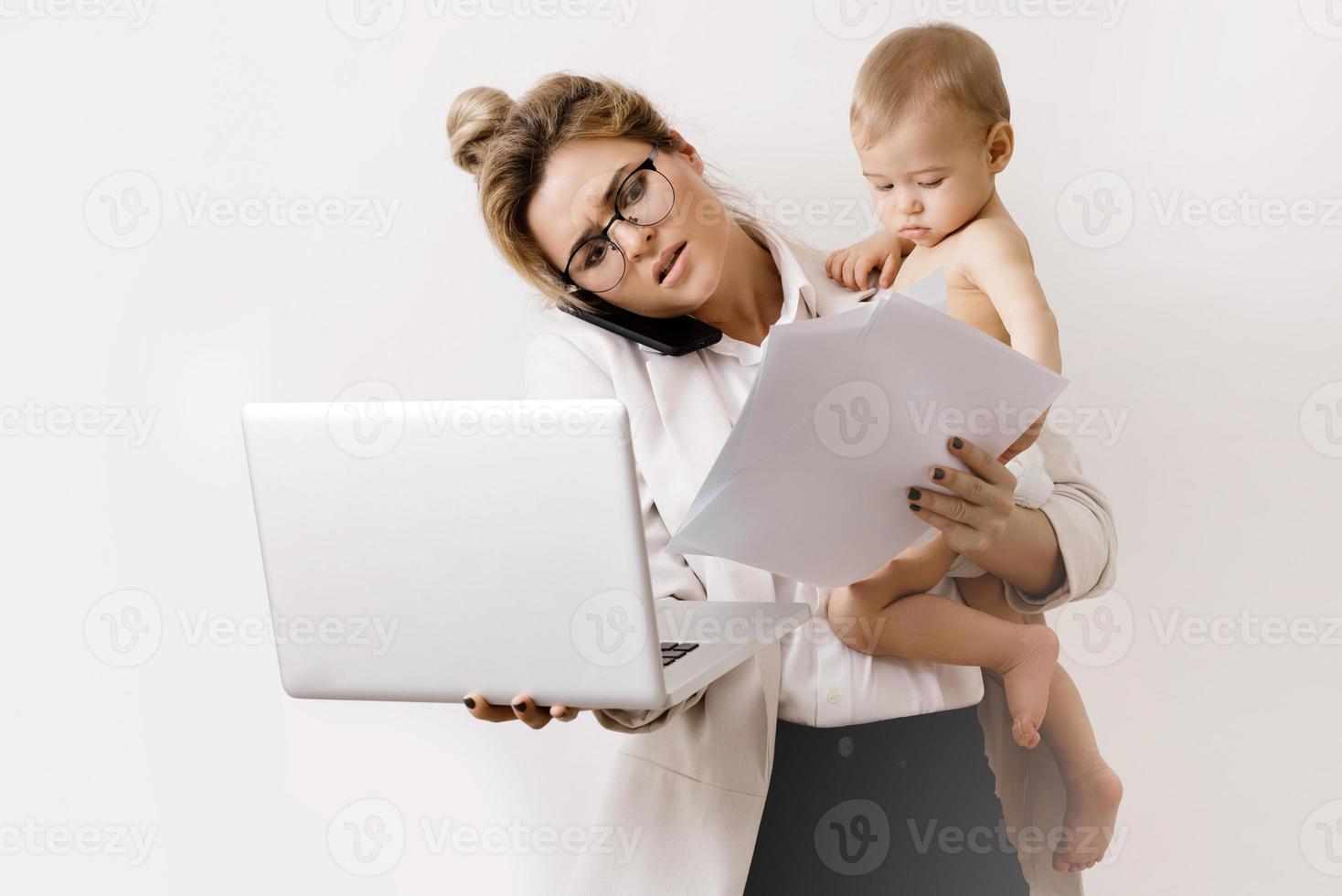 ung och upptagen affärskvinna är arbetssätt och innehav henne liten bebis foto
