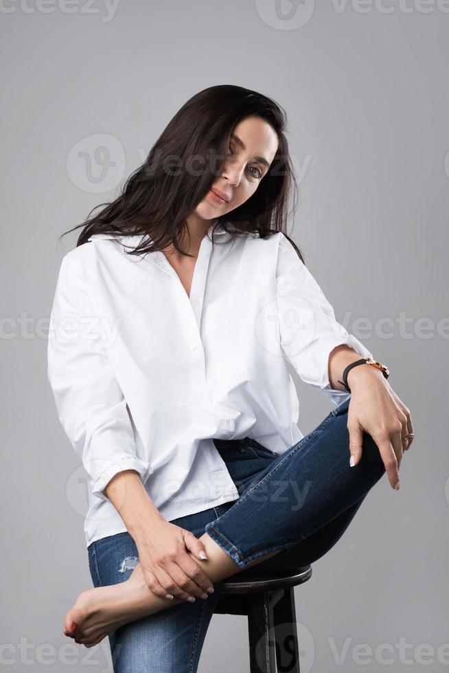 skön mitten åldrig mode modell bär vit skjorta och jeans i en Foto studio