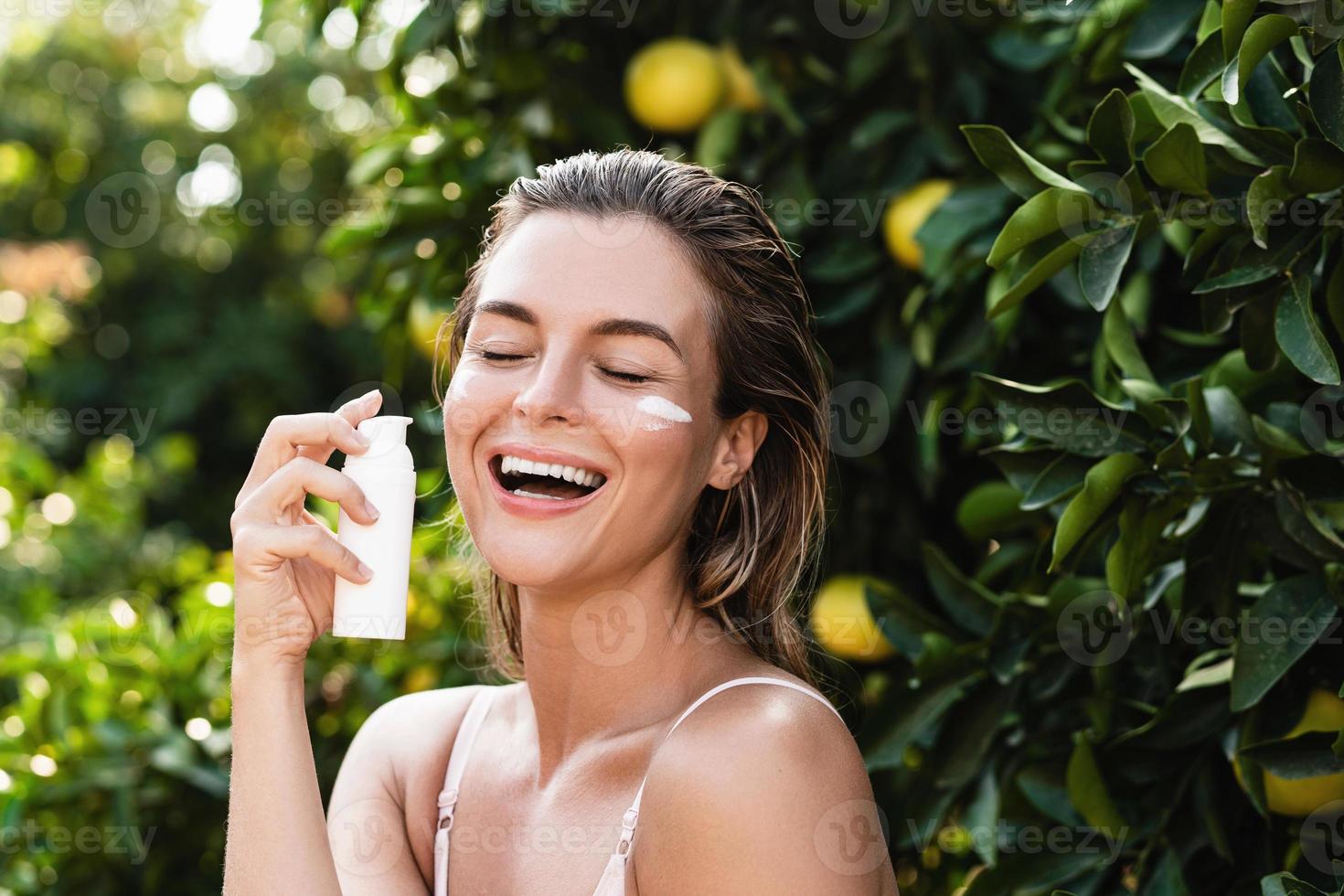 glad och skön kvinna applicering fuktgivande grädde eller solkräm på henne ansiktsbehandling hud foto