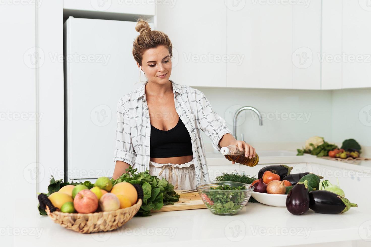 kvinna tillsats extra jungfrulig oliv olja till henne sallad under matlagning i vit kök foto