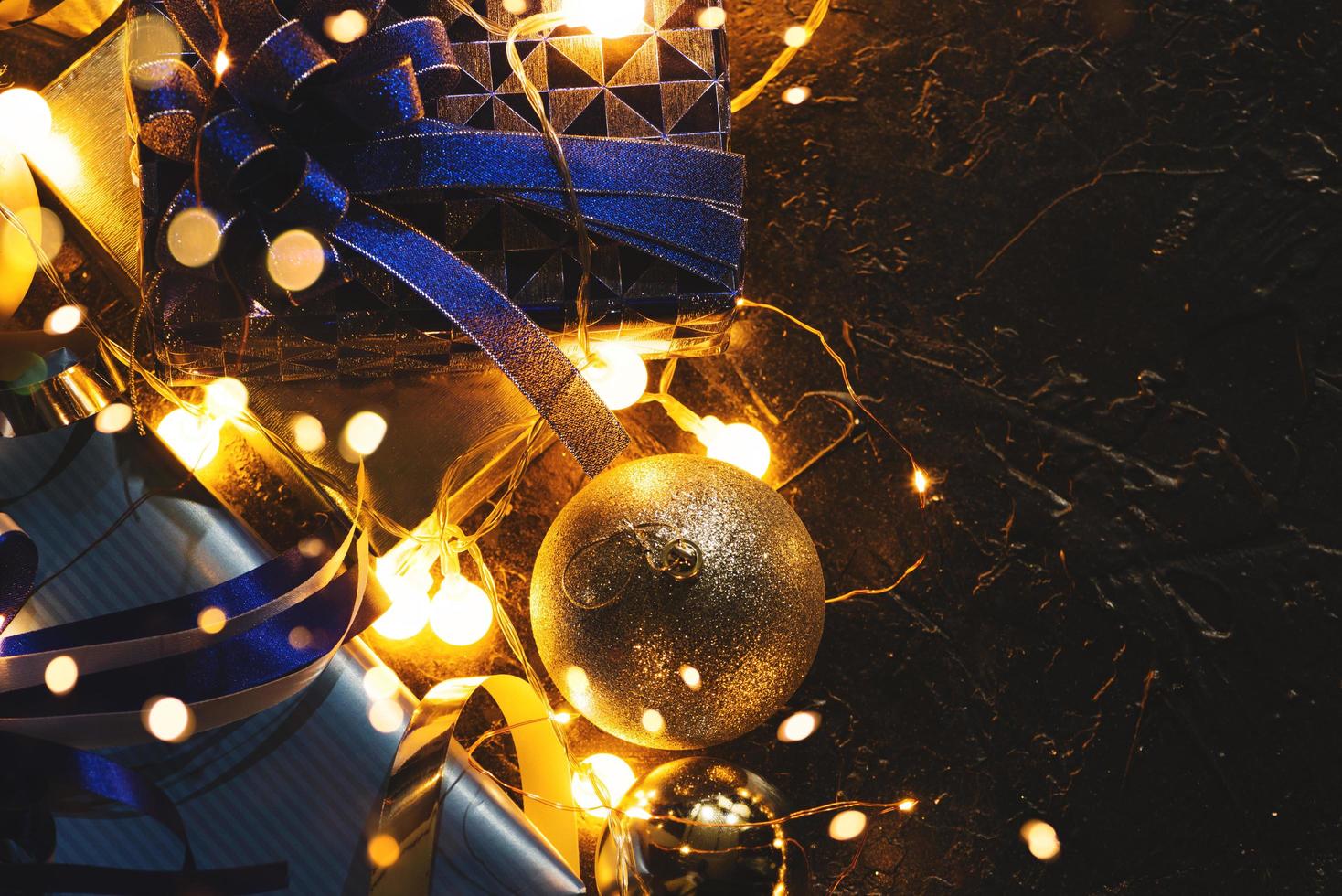 julklapp med blått band och juldekoration bollar på abstrakt bokeh svart bakgrund med kopia utrymme och dekorativa led-lampor. god jul och nytt år. foto