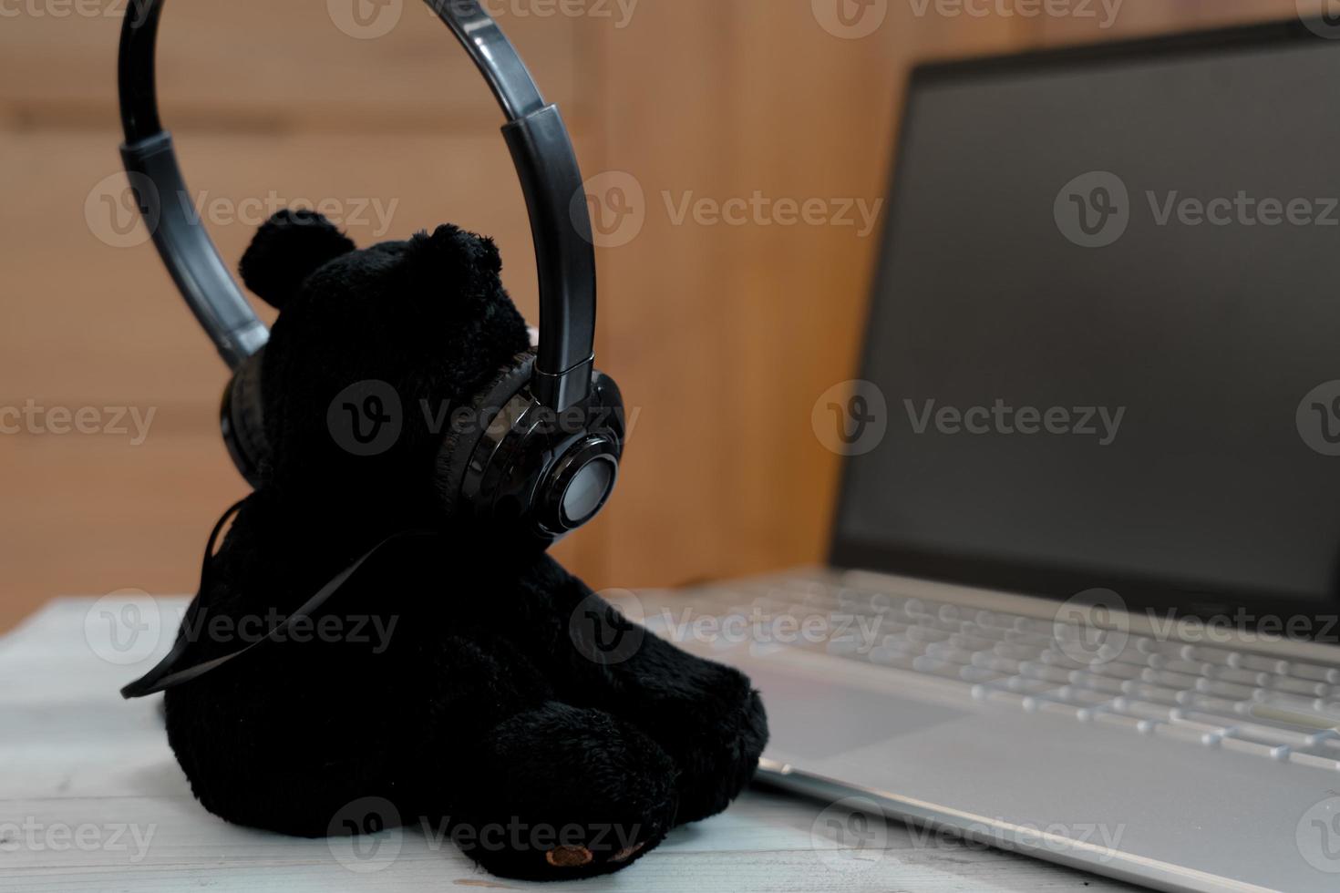 liten Björn bär hörlurar lyssna musik från bärbar dator, avkopplande tid. foto