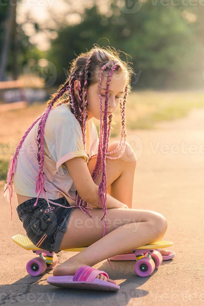 en Tonårs flicka med rosa pigtails sat ner på en penny styrelse och trodde. en flicka på en solig dag. foto