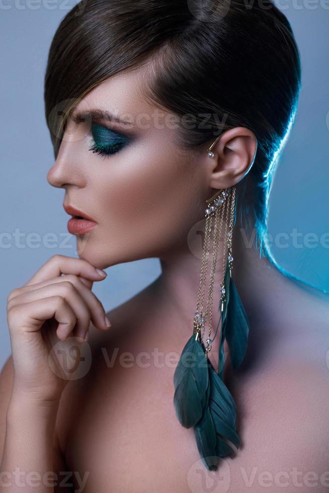 modell i eleganta bild med elegant hår beläggning ett öga och fjäder örhänge foto