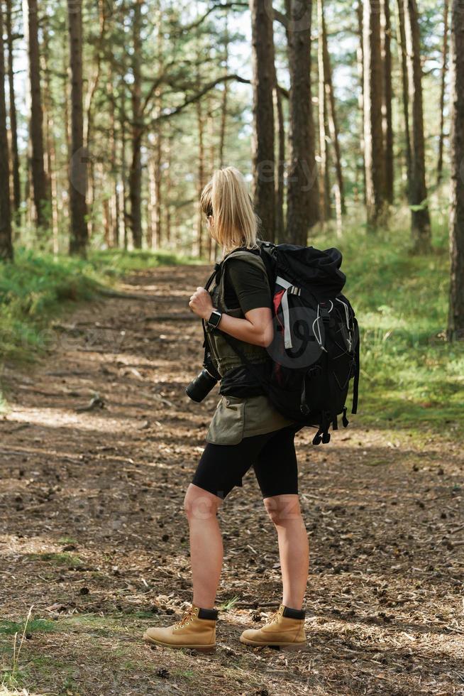 kvinna vandrare med stor ryggsäck i grön skog foto