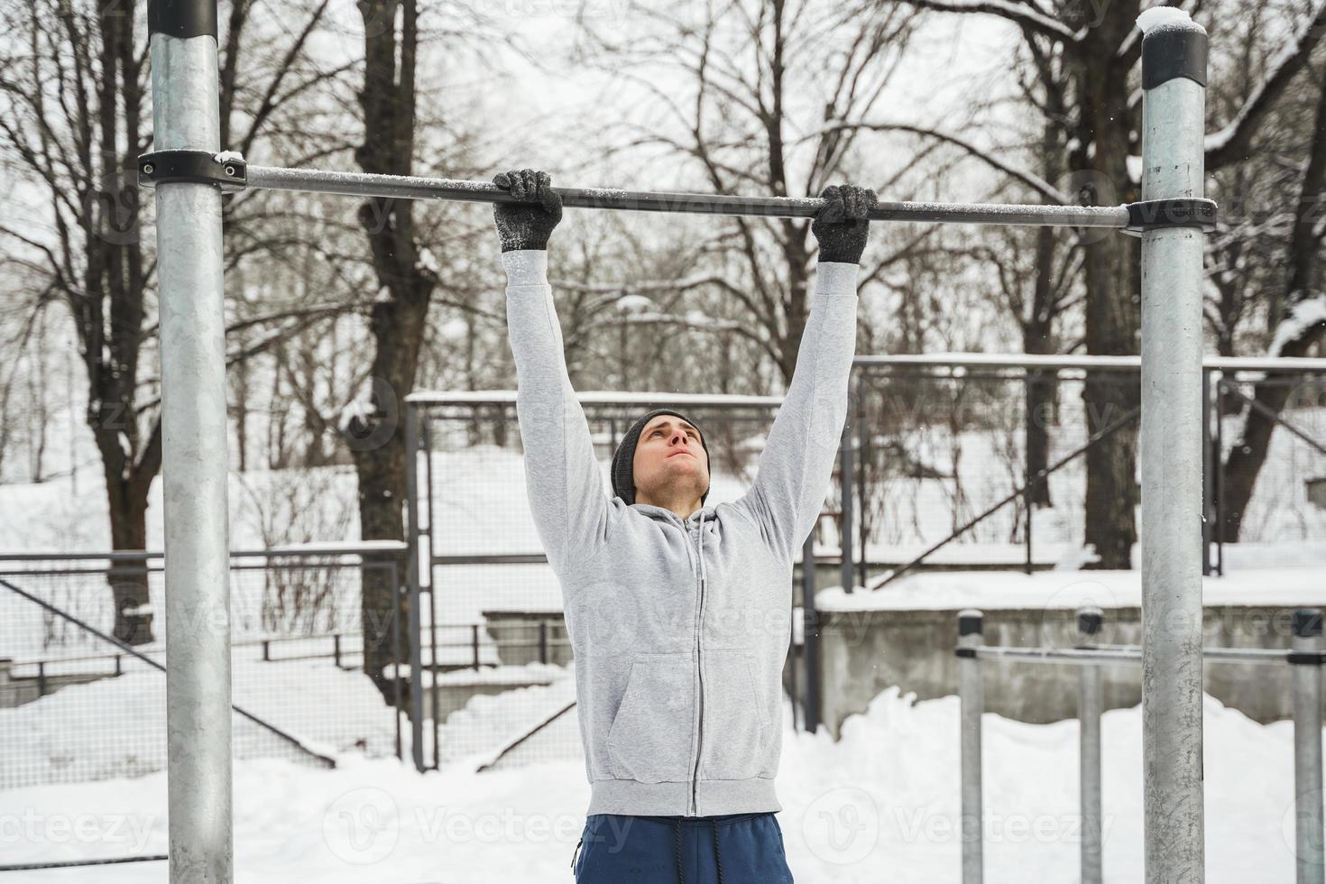atletisk man håller på med pull-ups på horisontell bar under hans utomhus- vinter- träna foto
