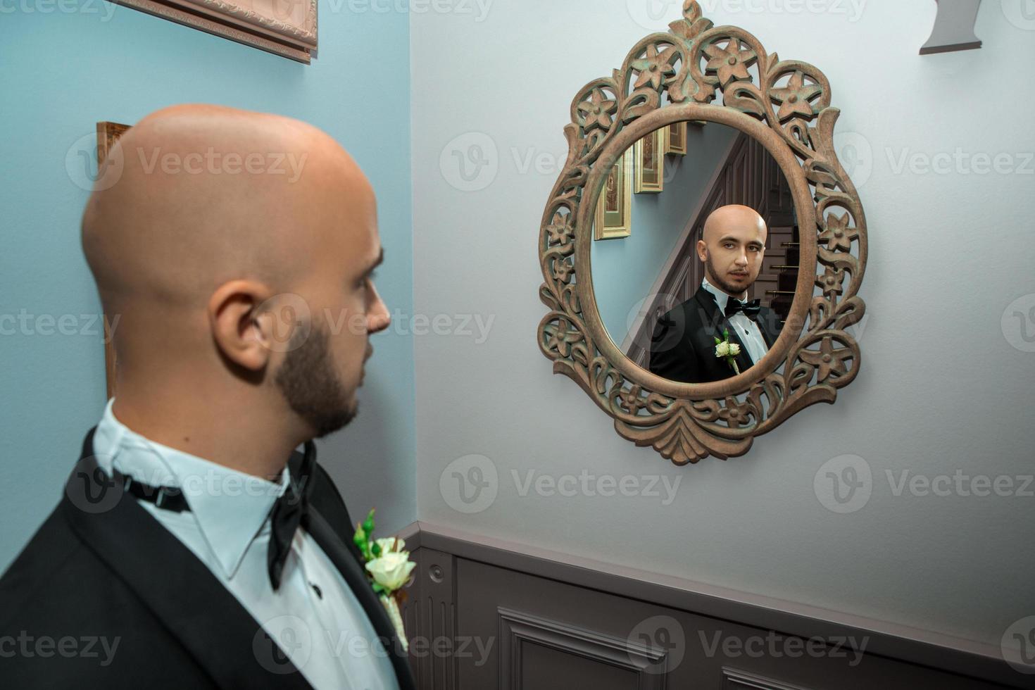 ung elegant brudgum ser på de spegel foto
