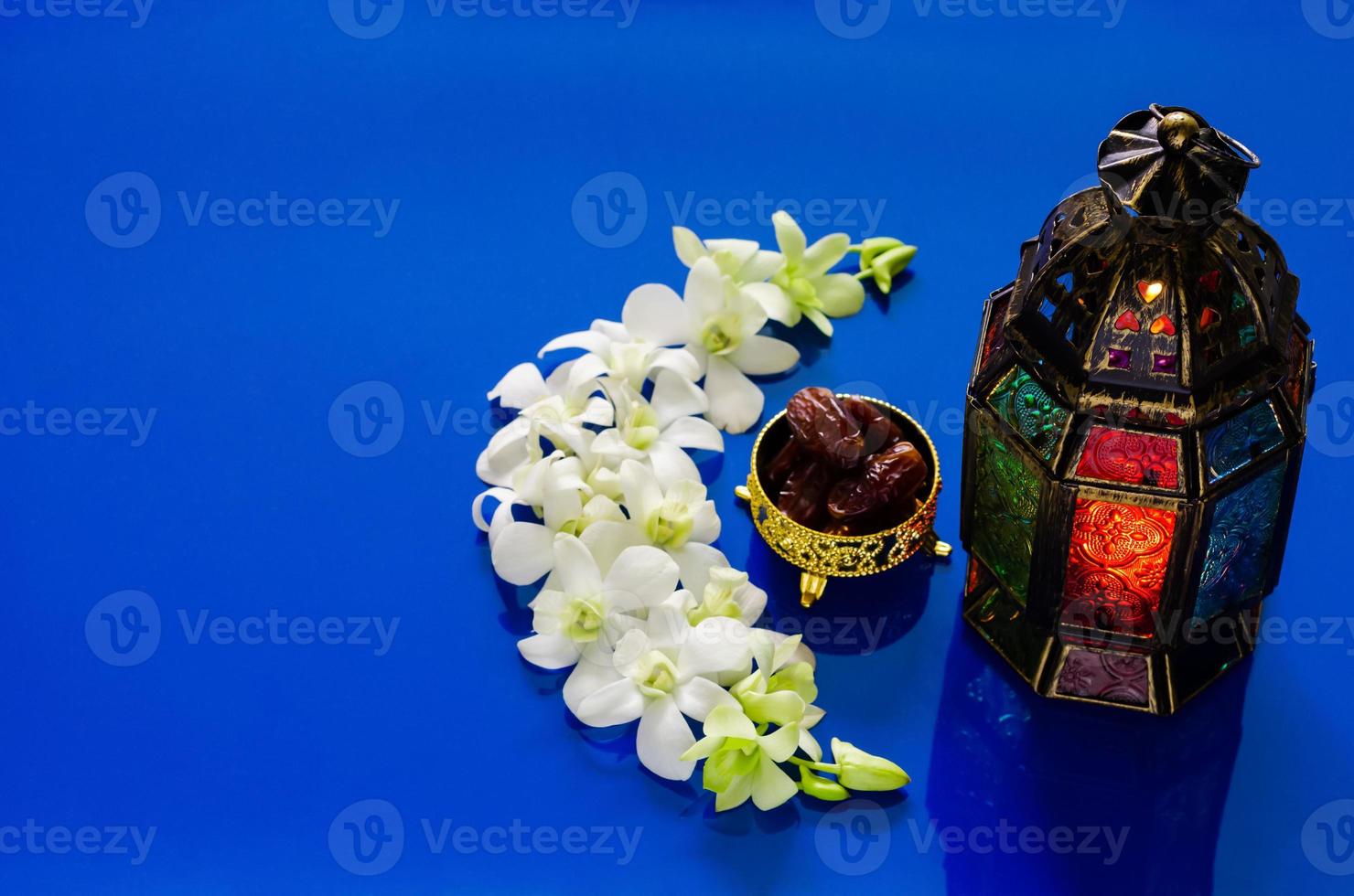 lykta på blå bakgrund med datum frukt på orkide blomma uppsättning som de halvmåne form för de muslim fest av de helig månad av ramadan kareem. foto