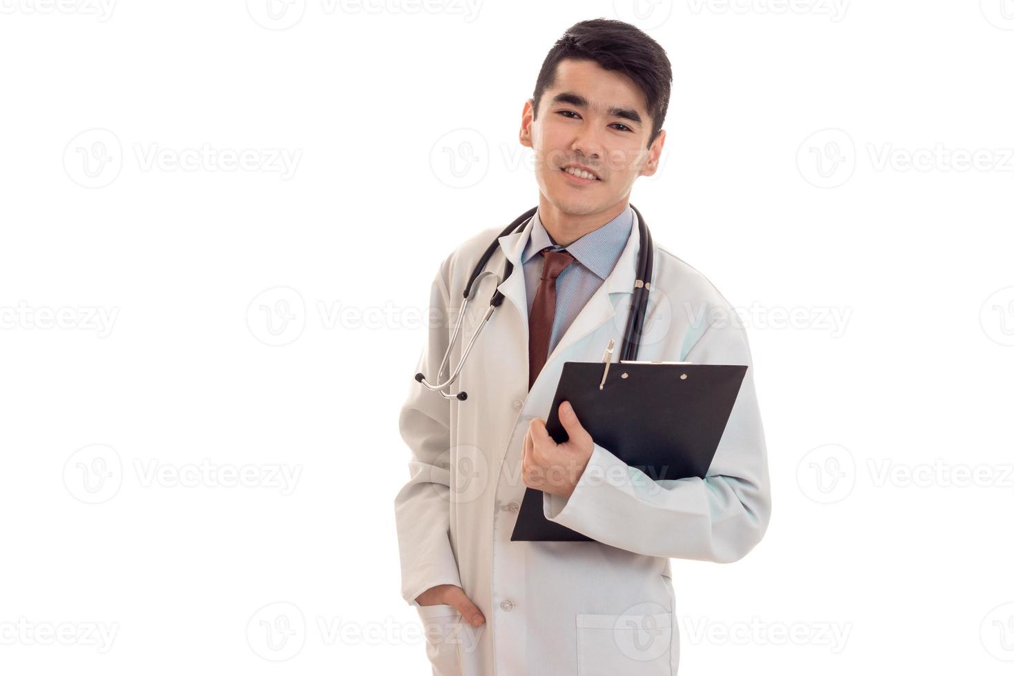 skön ung brunett man läkare i vit enhetlig med stetoskop ser på de kamera isolerat i studio foto