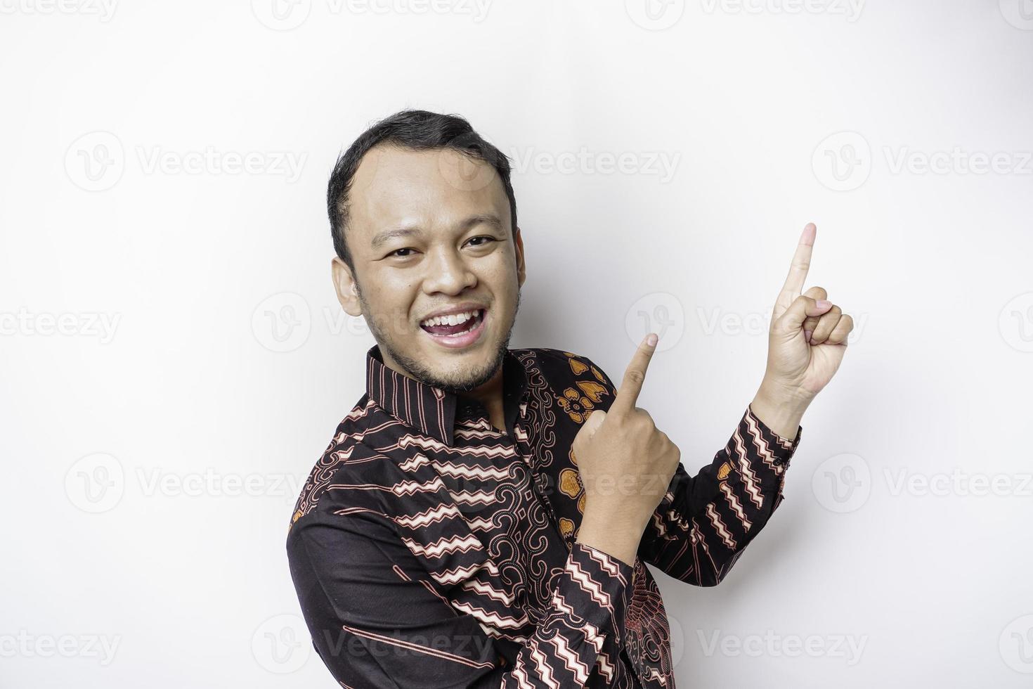 upphetsad asiatisk man bär batik skjorta pekande på de kopia Plats på topp av honom, isolerat förbi vit bakgrund foto