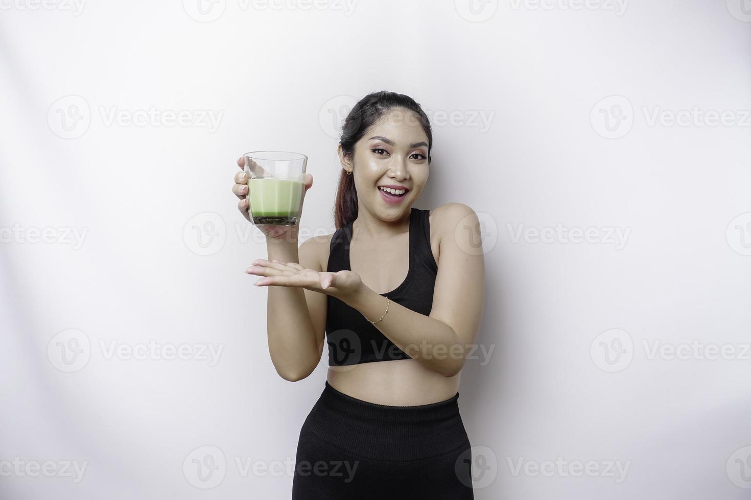 glad sportig asiatisk kvinna bär sportkläder med glas av gott grön smoothie, isolerat på vit bakgrund. foto