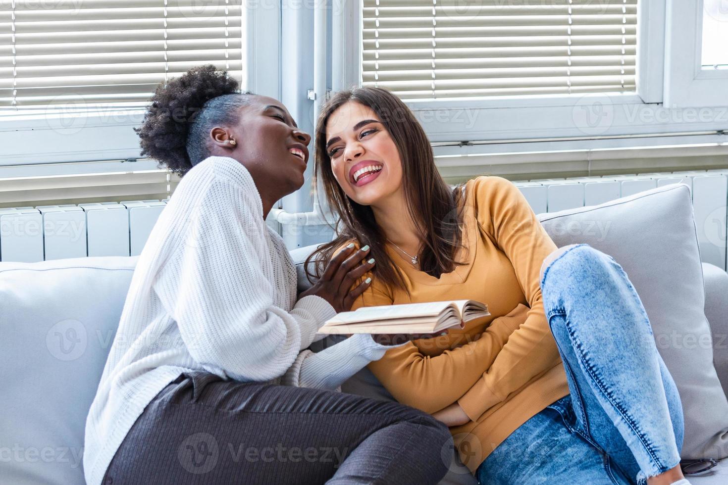 två kvinnor skrattande handla om rolig berättelser från böcker på Hem. vänskap och vård, Lycklig flicka vänner. afrikansk amerikan och caucasian bäst vänner foto