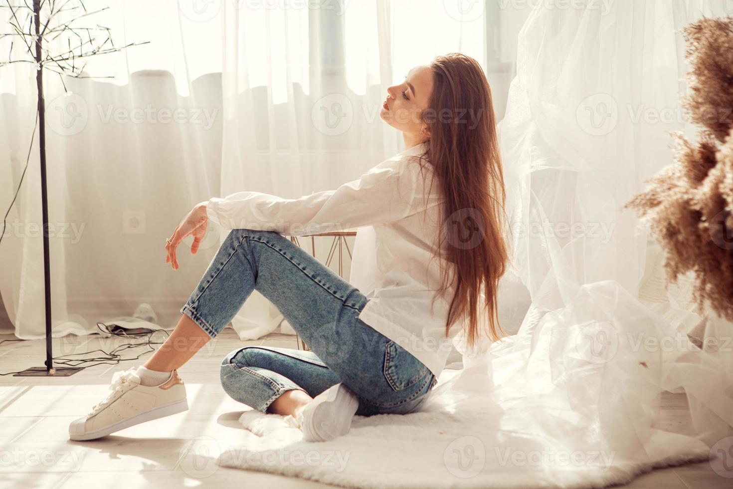 charmig kvinna sitter i främre av säng på ljus rum på Hem foto