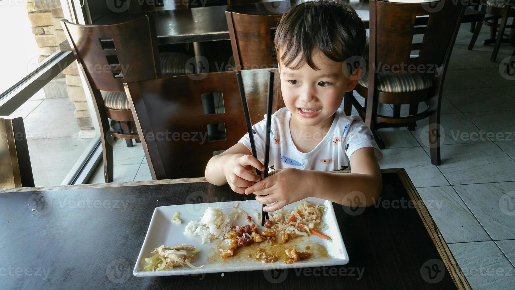 söt ung kinesisk och caucasian pojke inlärning till använda sig av ätpinnar på restaurang foto