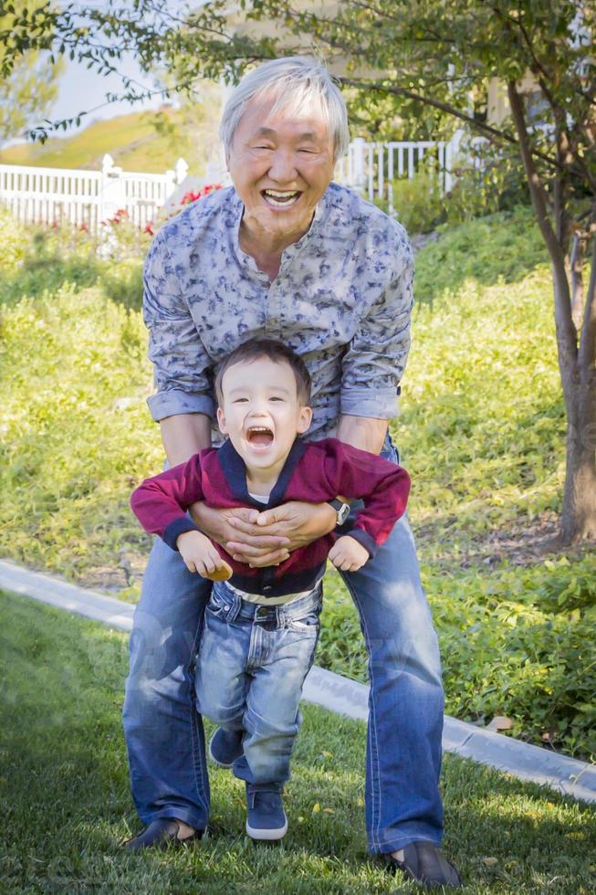 kinesisk morfar har roligt med hans blandad lopp barnbarn utanför foto