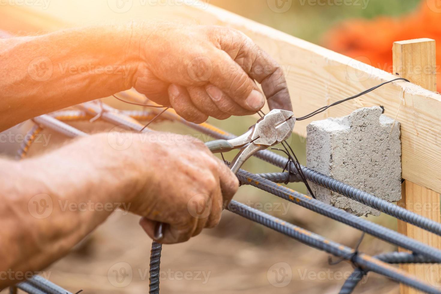arbetstagare säkring stål armeringsjärn inramning med tråd plier fräs verktyg på konstruktion webbplats foto