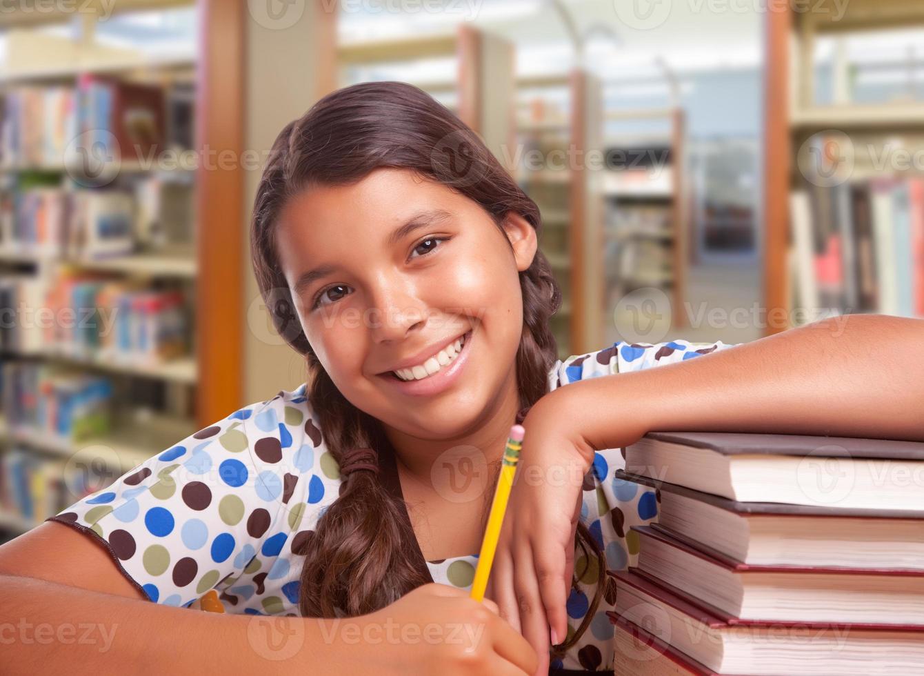 Lycklig latinamerikan flicka studerande med penna och böcker studerar i bibliotek foto