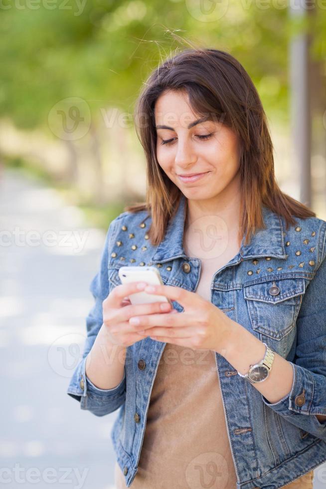 skön ung etnisk kvinna använder sig av henne smartphone utanför. foto