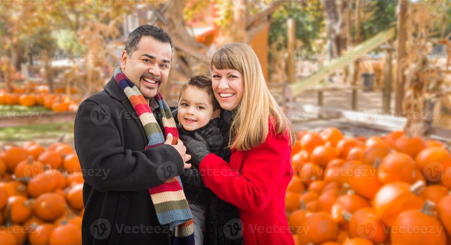 Lycklig biracial familj har roligt på de pumpa lappa odla. foto