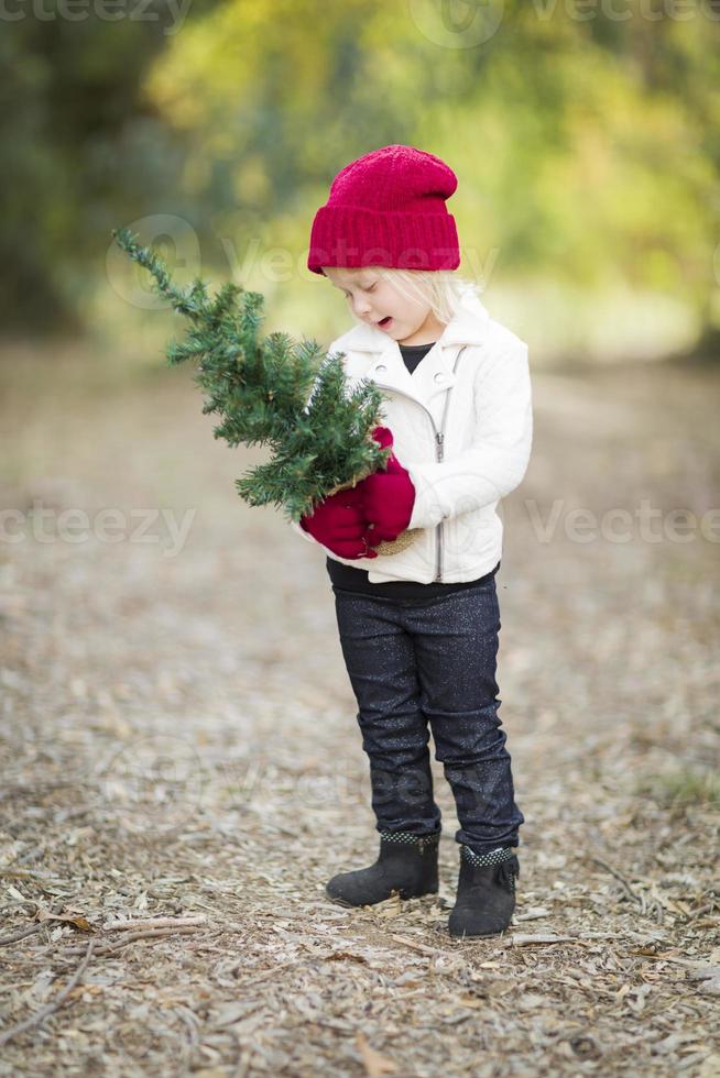 bebis flicka i röd vantar och keps innehav små jul träd foto