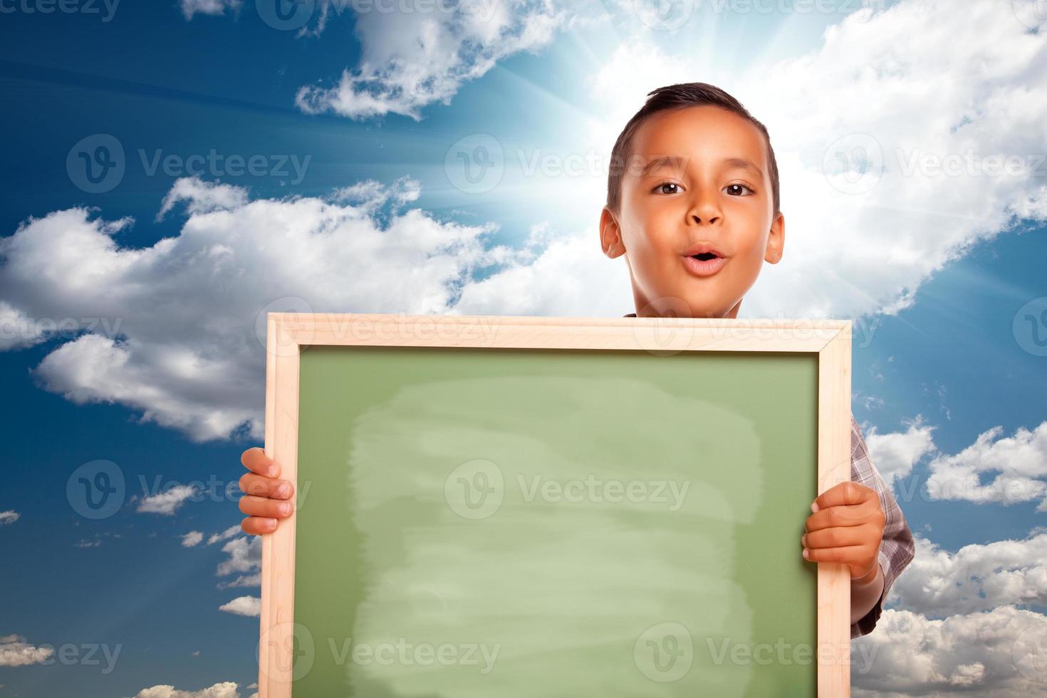 stolt latinamerikan pojke innehav tom svarta tavlan över himmel foto