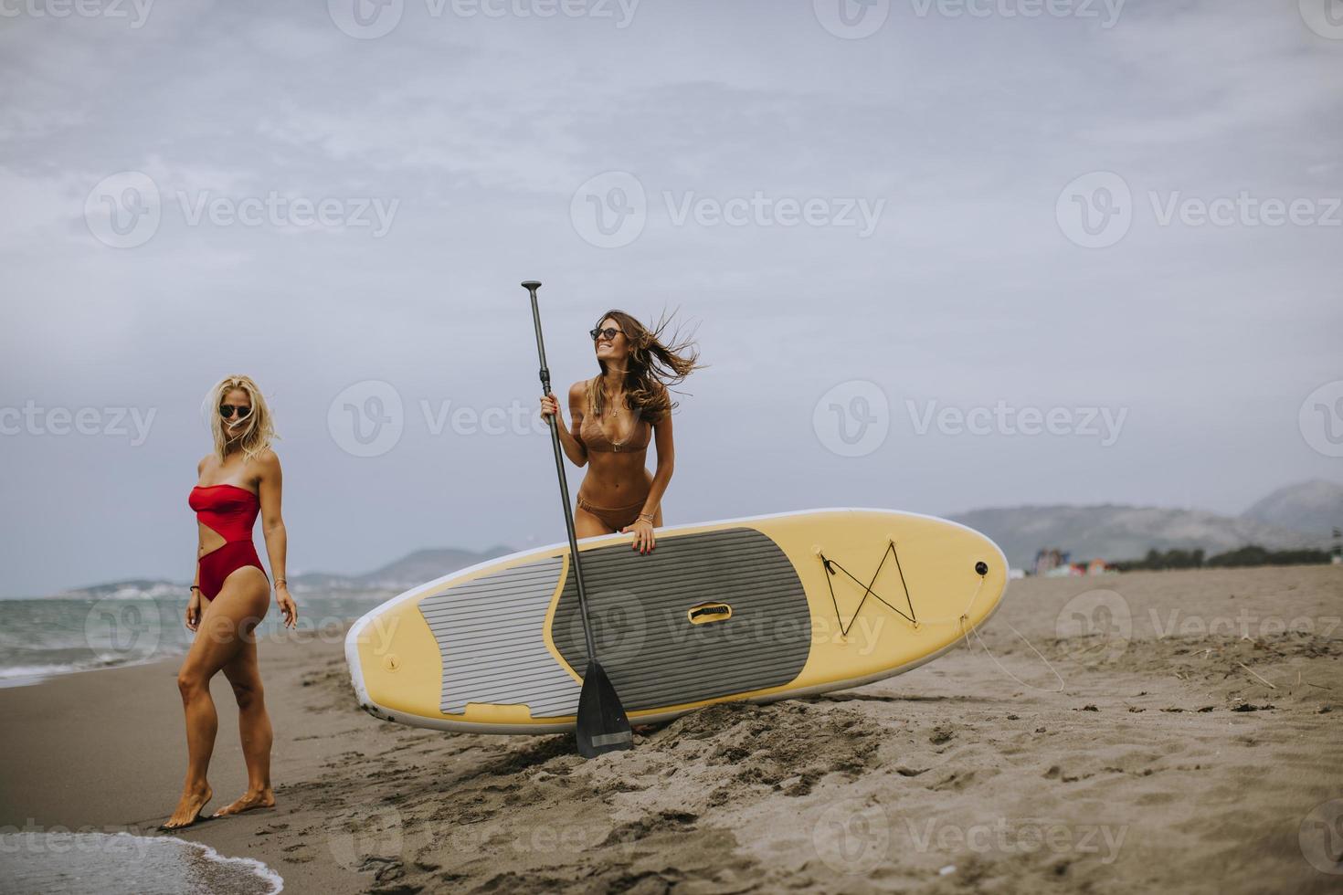 två unga kvinnor med paddelbräda på stranden en sommardag foto