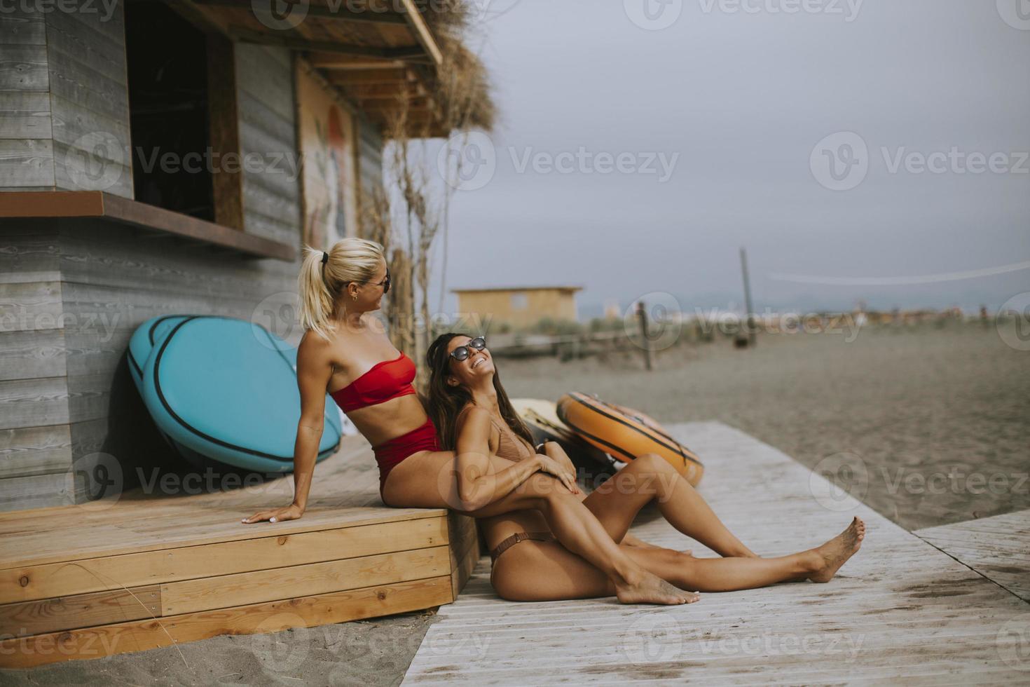unga kvinnor i bikini sitter vid surfstugan på en strand sommardag foto