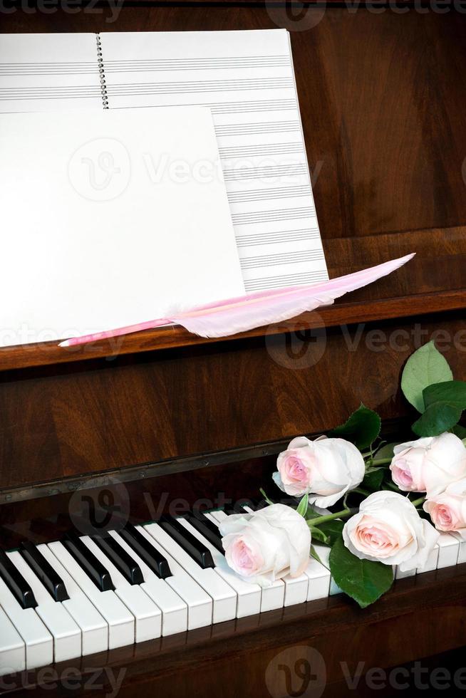 piano, blek rosa ro på tangentbord, musik papper och vit tom med rosa gåspenna penna. foto