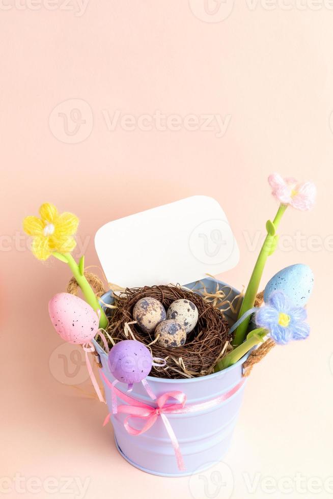 blå hink med bo av vaktel ägg, dekorativ ägg, blommor, tömma notera på pastell rosa. falsk upp. foto
