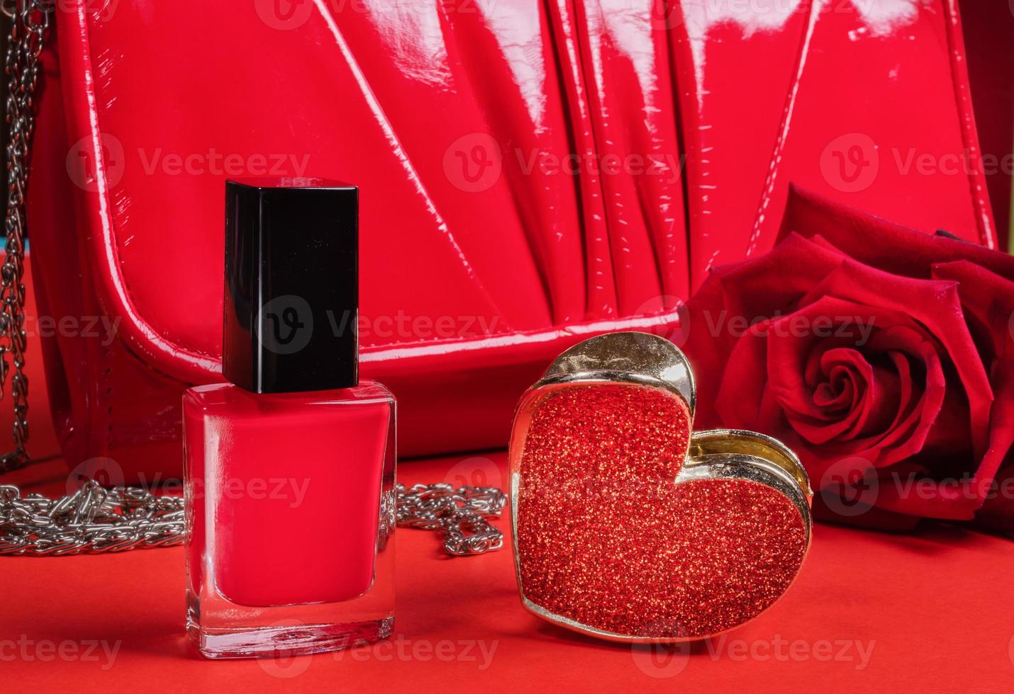 stänga upp uppsättning av kvinna röd objekt nagel putsa, hår klämma, handväska och reste sig på röd bakgrund. foto