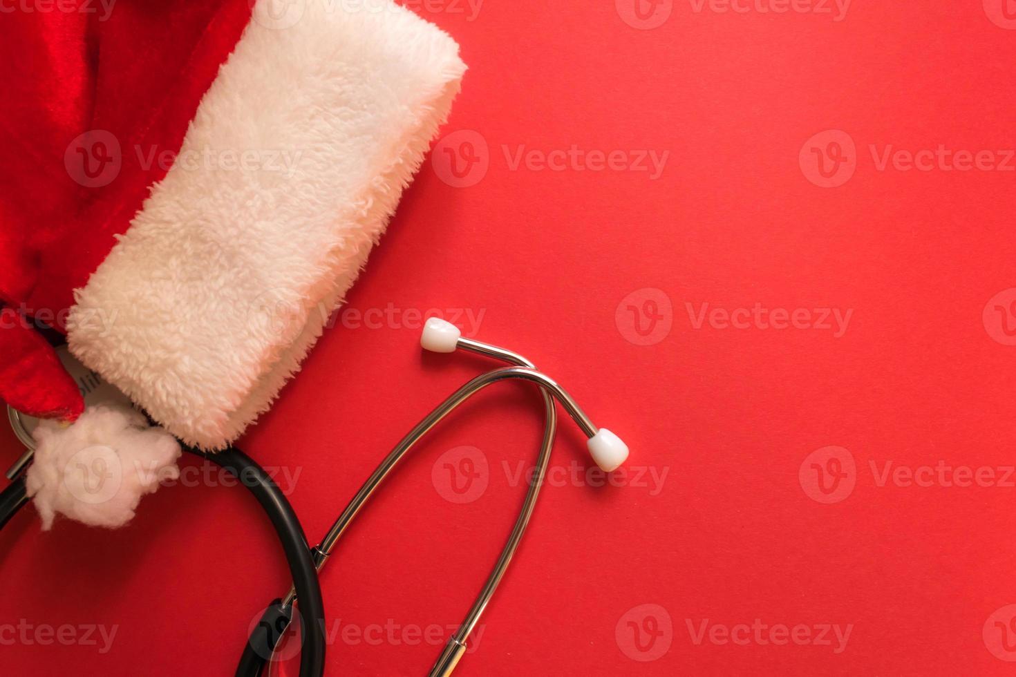 medicinsk jul och ny år sammansättning med stetoskop och santa hatt på röd bakgrund. hälsa vård och medicin begrepp för kort, kalender, omslag. foto