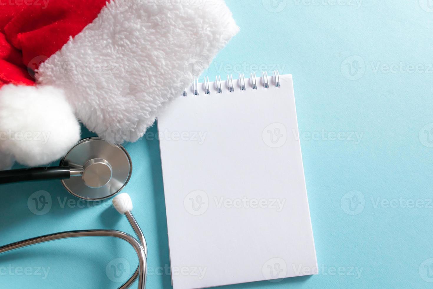 medicinsk jul och ny år sammansättning med stetoskop, anteckningsblock och santa hatt på blå bakgrund. hälsa vård och medicin begrepp för kort, kalender, omslag. foto