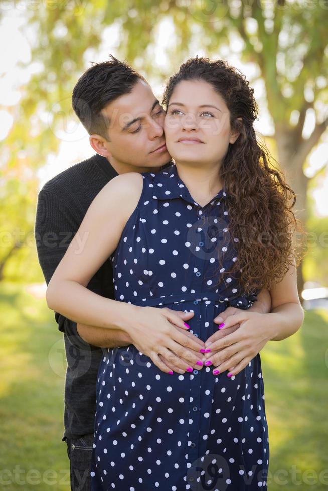 latinamerikan man kramar hans gravid fru utomhus på de parkera foto