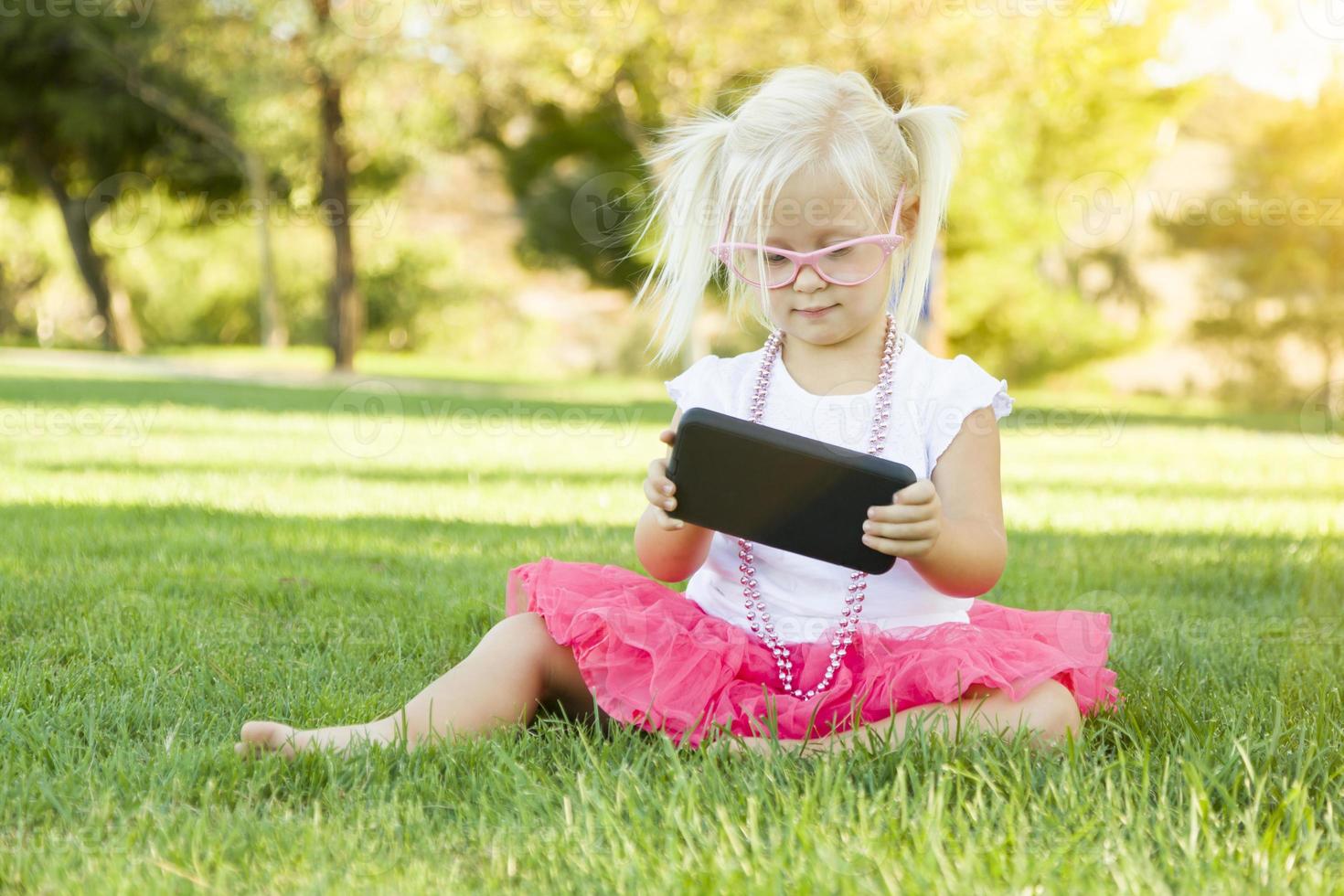 liten flicka i gräs spelar med cell telefon foto