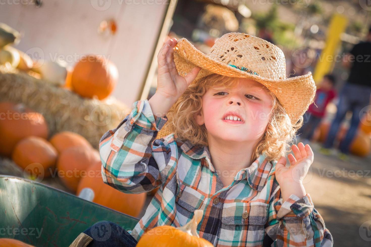 liten pojke Sammanträde med en cowboy hatt i en rustik ranch miljö på de pumpa lappa. foto