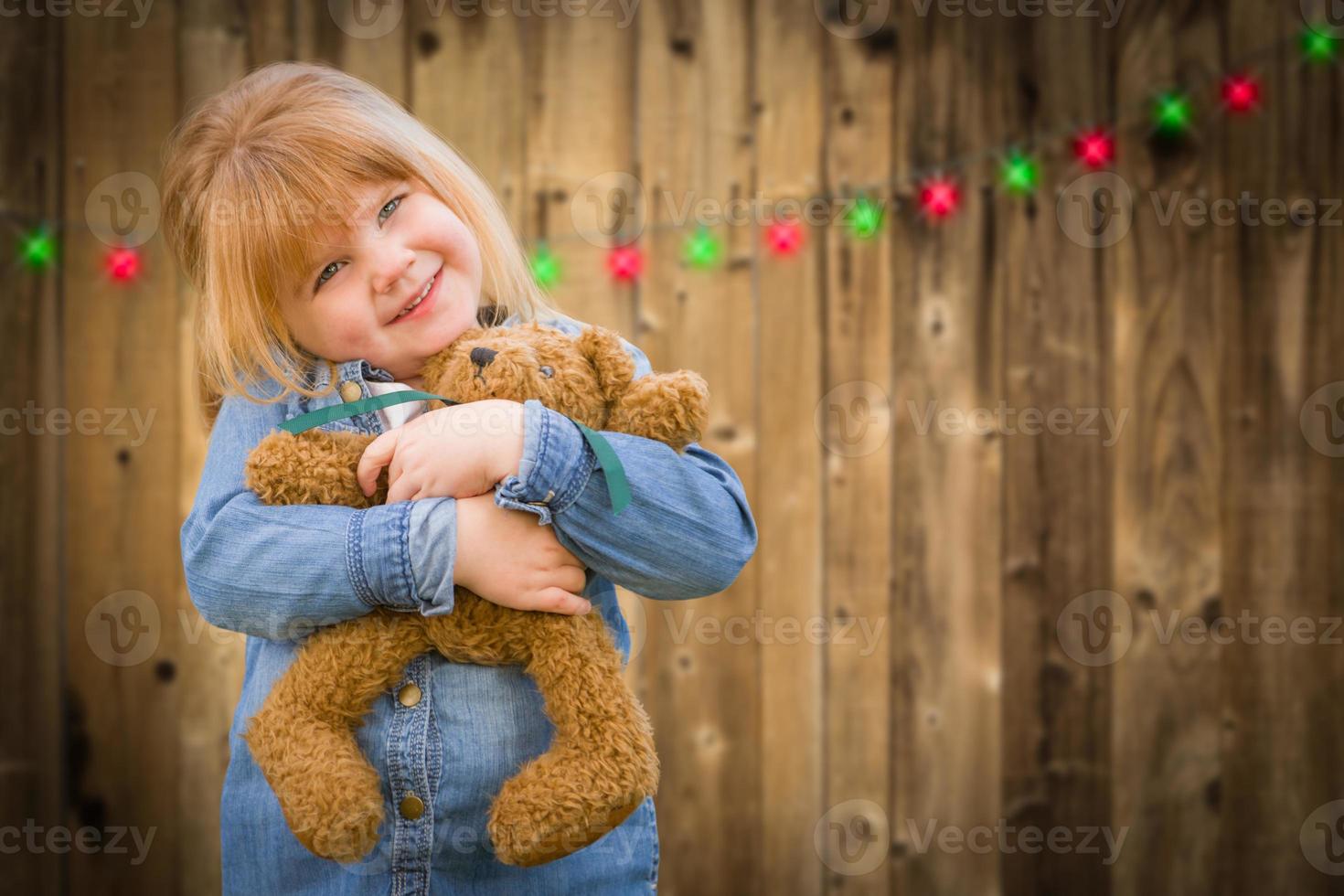 flicka innehav teddy Björn i främre av trädbevuxen bakgrund med jul lampor foto