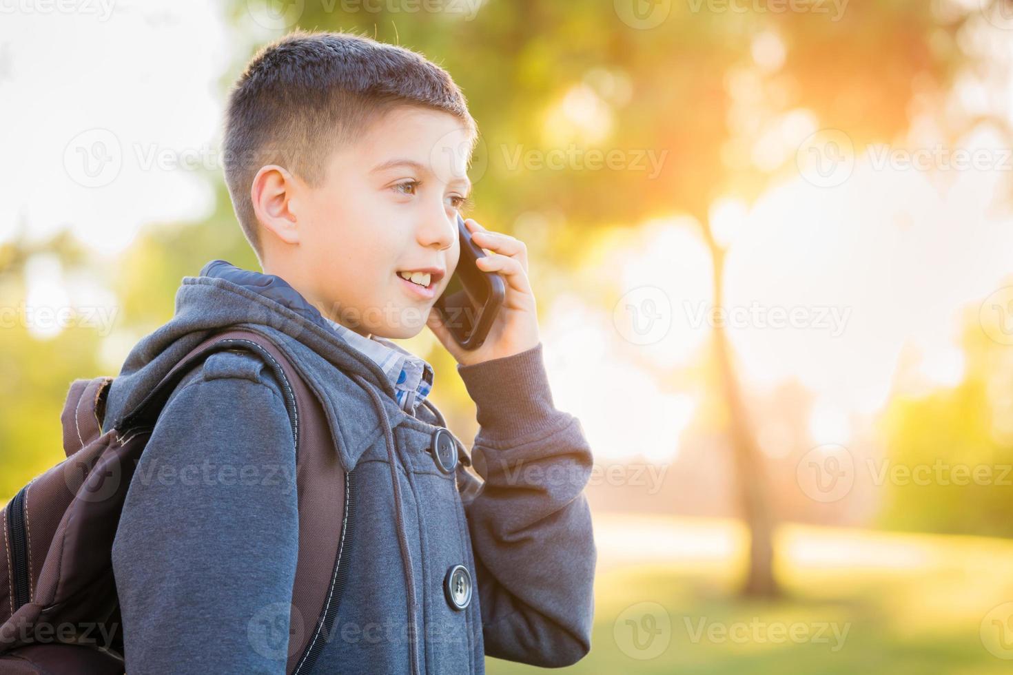 ung latinamerikan pojke gående utomhus med ryggsäck talande på cell telefon foto