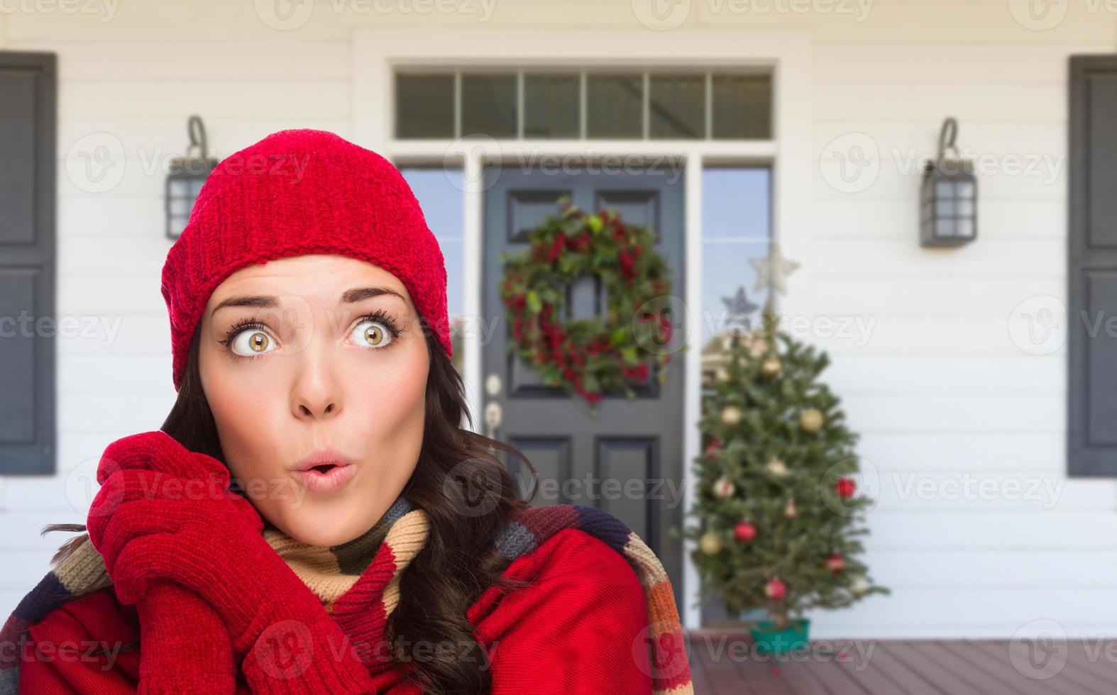 ung flicka bär scarf, röd keps och vantar stående på jul dekorerad främre veranda foto