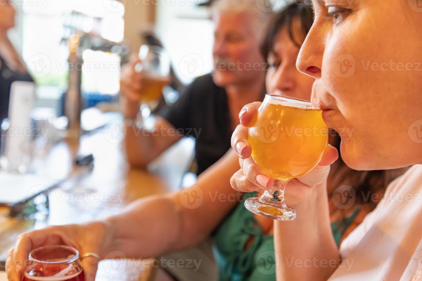 kvinna smuttar glas av mikro brygga öl på bar med vänner foto