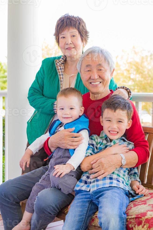 senior vuxen kinesisk par Sammanträde med deras blandad lopp barnbarn foto