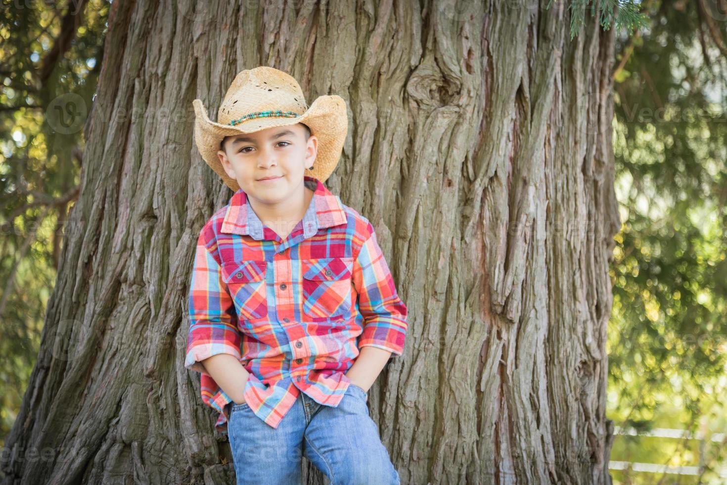 blandad lopp ung pojke bär cowboy hatt stående utomhus. foto